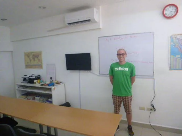 Luke in a green shirt standing in front of a classroom whiteboard for the first time